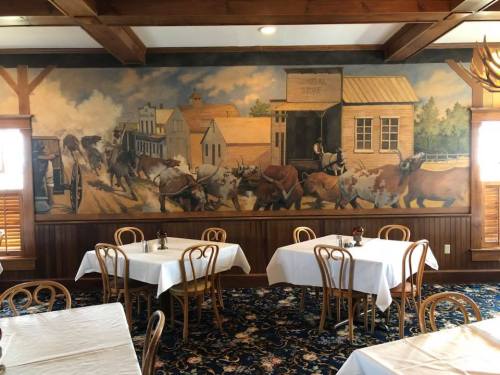 A cozy restaurant interior featuring tables with white tablecloths and a mural of a historic town scene on the wall.