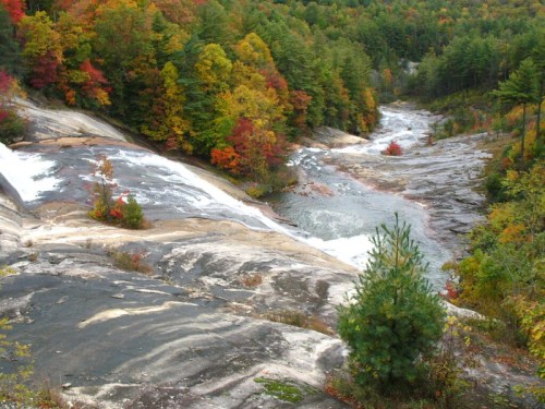A scenic view of a waterfall cascading over smooth rocks, surrounded by vibrant autumn foliage and lush green trees.