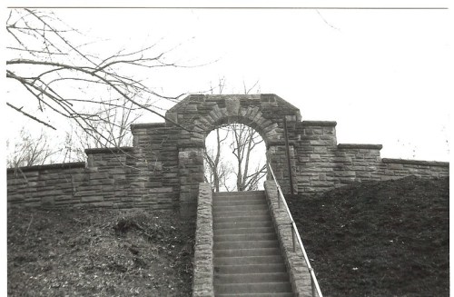 A stone archway atop a set of stairs, surrounded by bare trees in a black and white setting.