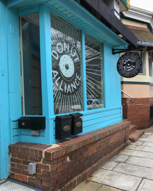 Exterior of a blue building with "Donut Alliance" sign and large window graphic featuring a donut design.