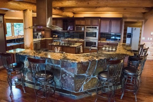 A spacious kitchen with dark wood cabinets, granite countertops, and a stone bar with high stools.