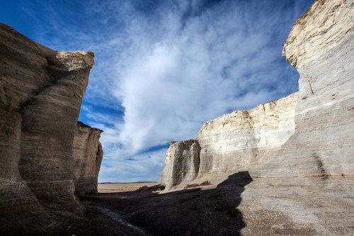 A dramatic landscape featuring towering rock formations under a blue sky with scattered clouds.