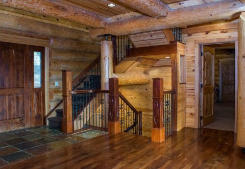 A rustic log cabin interior featuring a wooden staircase, stone flooring, and warm wooden walls.