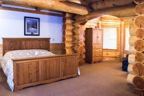 Cozy log cabin bedroom featuring a wooden bed, dresser, and natural wood accents. Warm, inviting atmosphere.