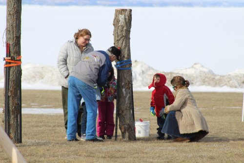 A group of adults and children gather around a tree, preparing for an outdoor activity in a snowy landscape.