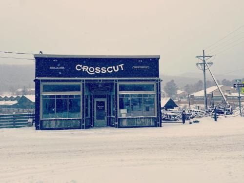 A snow-covered storefront labeled "CROSSCUT" in a winter landscape, with snow falling and a quiet street.