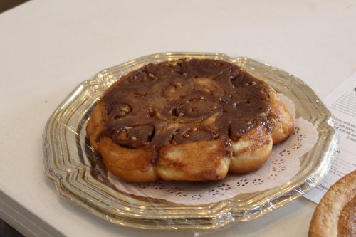 A round cinnamon roll topped with chocolate and nuts, served on a decorative glass plate.
