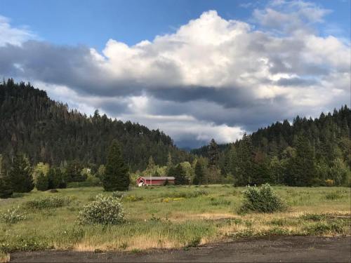 A red barn sits in a green field surrounded by trees and mountains under a cloudy sky.