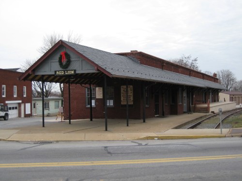 Historic train station with a red brick exterior, a sloped roof, and a festive wreath on the sign reading "Red Lion."