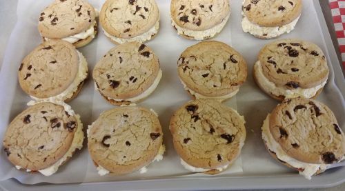 A tray of chocolate chip cookie sandwiches filled with cream, arranged neatly on parchment paper.