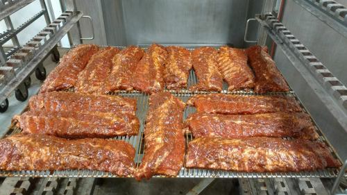 A rack of glazed barbecue ribs cooking on a grill, arranged neatly in rows.