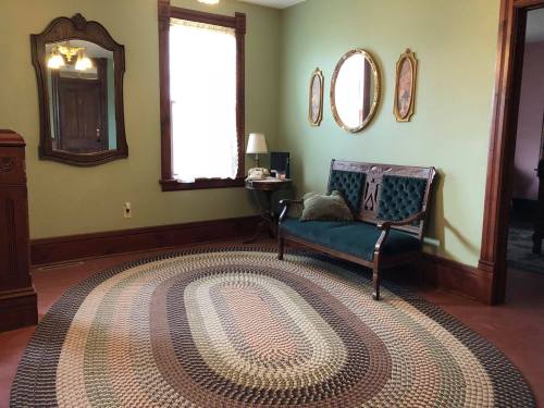 Cozy room with green walls, a vintage sofa, round braided rug, and mirrors, featuring warm natural light.