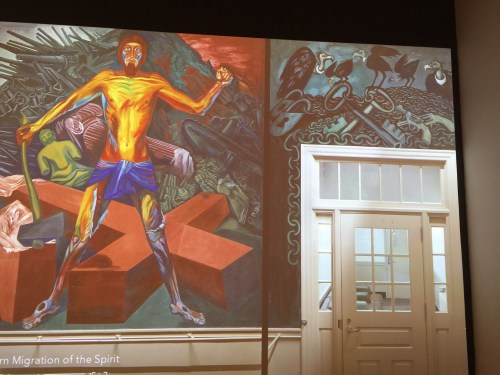 A vibrant mural depicting a figure with a hammer, surrounded by abstract shapes and dark imagery, next to a doorway.
