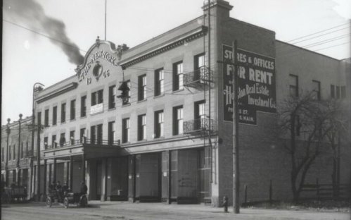 Historic building with a sign for "For Rent," featuring a classic architectural style and early 20th-century vehicles.