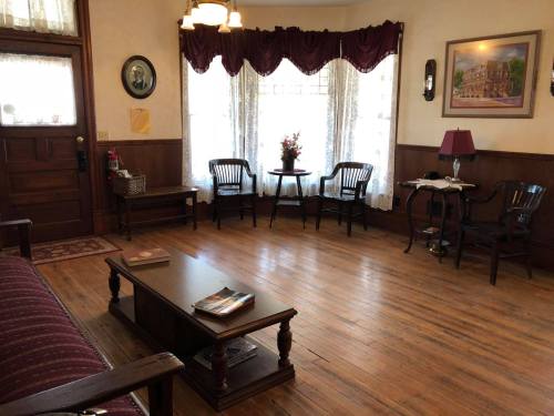 Cozy living room with wooden floors, a coffee table, chairs, and large windows with lace curtains.