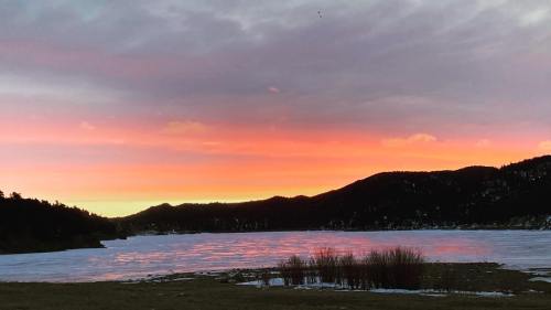 A serene lake at sunset, with vibrant pink and orange skies reflecting on the icy water and mountains in the background.