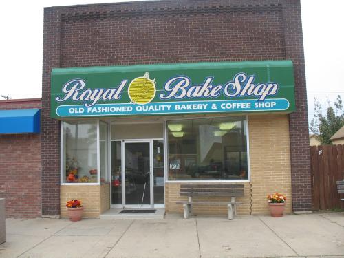 Exterior of Royal Bake Shop, featuring a green sign, large windows, and a welcoming entrance with flower pots.