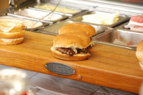 A close-up of a hamburger on a wooden serving board, with additional burger buns in the background.