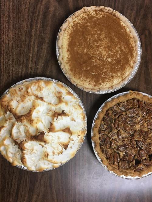 Three pies on a wooden table: a coconut cream pie, a pecan pie, and a pie with a cinnamon topping.