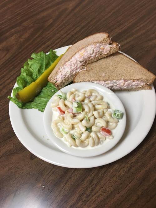 A plate with two slices of sandwich, a pickle, lettuce, and a side of macaroni salad.
