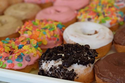 A variety of colorful donuts with sprinkles, frosting, and toppings arranged on a tray.