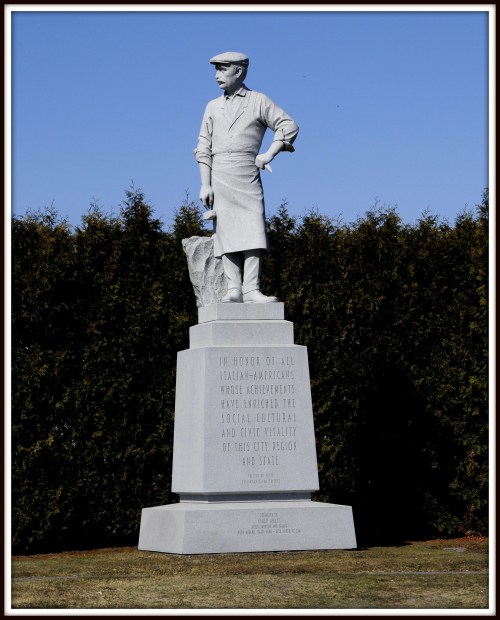 Statue honoring Italian-Americans, depicting a man in work attire, with an inscription on the pedestal.