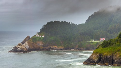 A coastal scene featuring a lighthouse on a rocky shore, surrounded by lush green hills and misty skies.