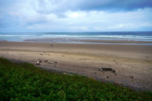 A serene beach scene with gentle waves, a sandy shore, and a cloudy sky, featuring a couple walking in the distance.