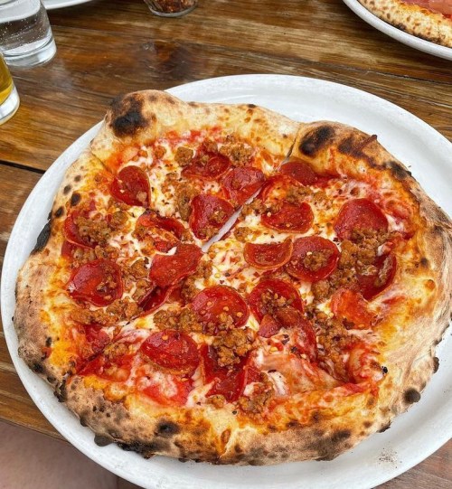 A freshly baked pizza topped with pepperoni and crumbled sausage on a wooden table.