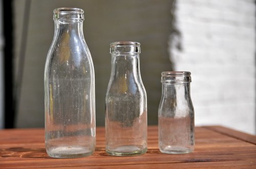 Three clear glass bottles of varying heights on a wooden surface, with a blurred background.