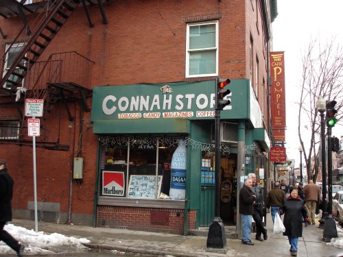A street view of Connah's Store, a brick building with a green awning, featuring signs for tobacco, candy, and coffee.