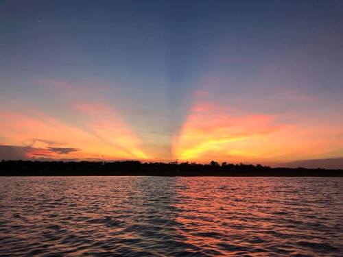 A serene sunset over water, with vibrant orange and pink hues illuminating the sky and reflecting on the surface.
