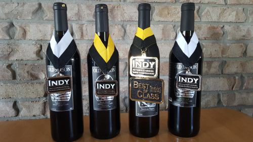Four wine bottles with medals hanging from their necks, showcasing awards for "Best of Class" and "Indy."