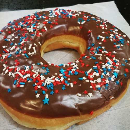 A chocolate frosted donut topped with red, white, and blue star-shaped sprinkles on a paper napkin.
