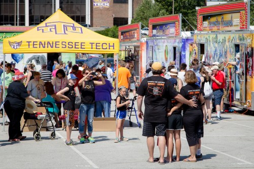 A lively outdoor event with food trucks and people enjoying the festivities, including a group posing for a photo.