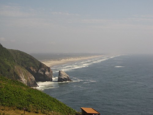 A scenic view of a coastline with rocky formations, sandy beach, and gentle waves under a hazy sky.