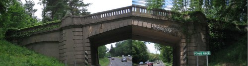 A stone bridge with greenery, spanning over a road, featuring a sign for "Ponus Ridge" nearby.