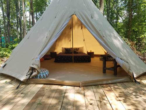 A cozy tent with a wooden floor, featuring cushions and a bed, set in a lush forest environment.