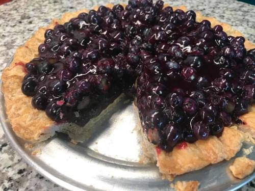 A freshly baked blueberry pie with a golden crust, partially sliced, showcasing a glossy filling of blueberries.