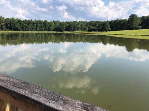A serene lake reflecting clouds and trees, with a wooden railing in the foreground.