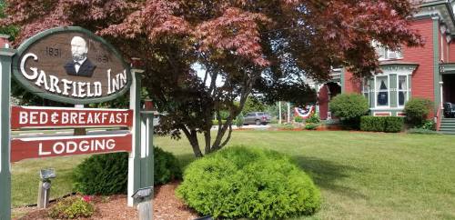Sign for Garfield Inn Bed & Breakfast with a historic building and landscaped yard, featuring a tree and decorative elements.