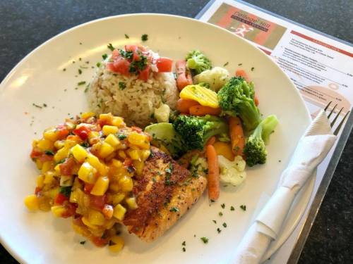 A plate featuring grilled salmon topped with mango salsa, served with rice and a side of mixed vegetables.