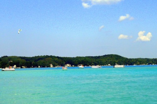 A serene lake scene with boats on turquoise water and a lush green shoreline under a clear blue sky.