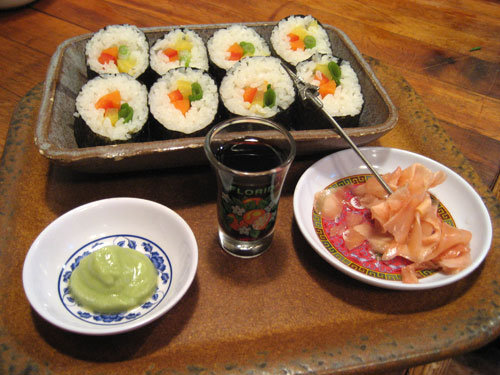 A tray with sushi rolls, wasabi, pickled ginger, and a shot glass of soy sauce.