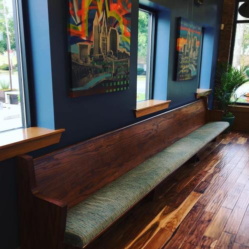 A wooden bench with a green cushion against a blue wall, featuring colorful artwork and large windows.