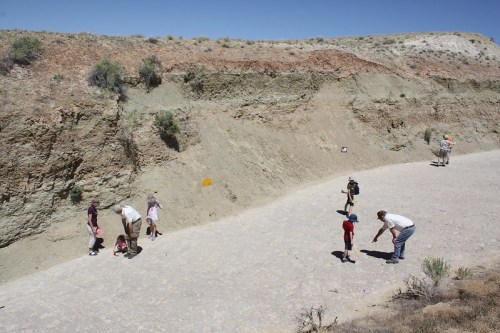 A group of children and adults explore a dry, rocky landscape under a clear blue sky.