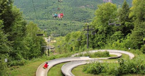 A scenic view of a summer luge track winding through green hills, with a chairlift in the background.