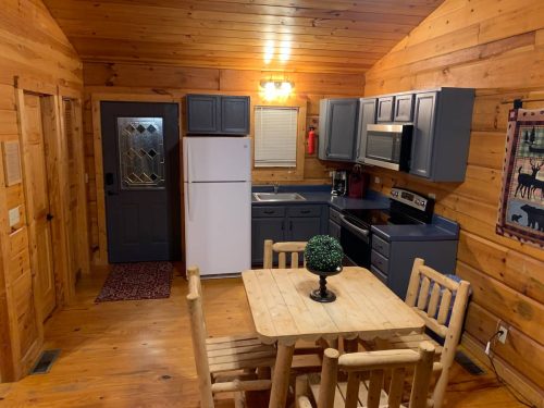 Cozy wooden kitchen with a dining table, refrigerator, stove, and rustic decor. Warm lighting enhances the inviting atmosphere.