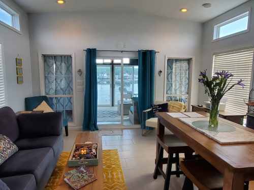 Cozy living space with a view of water, featuring a sofa, dining table, and large windows with blue curtains.