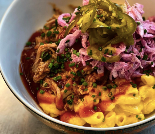 A bowl of macaroni and cheese topped with pulled pork, pink slaw, jalapeños, and green onions.